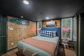 A bedroom with a bed, a wall-mounted air conditioner, and a window with blinds.