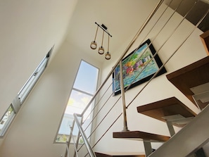 Stunning staircase with glass railings and a large window, flanked by a vibrant painting.
