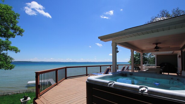 Ein Whirlpool auf einer Holzterrasse mit Blick auf ein Gewässer und einen klaren Himmel.