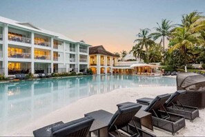 Relax by the pool surrounded by lounge chairs and umbrellas, with a hotel building in the background.