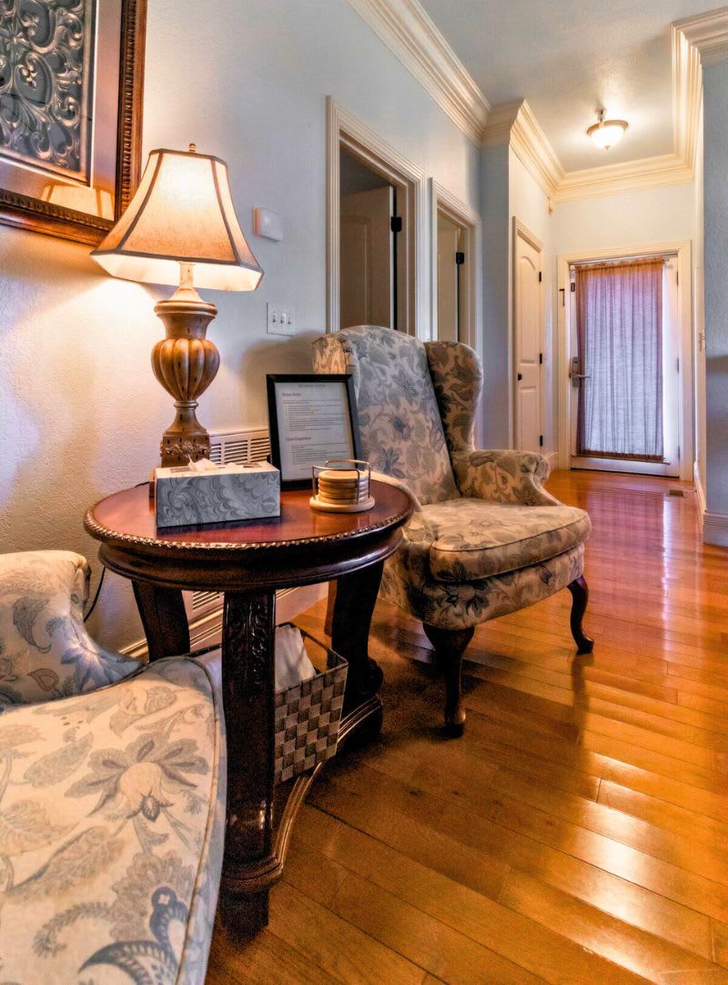 Een woonkamer met een ronde houten tafel, twee gestreepte fauteuils, een lamp en een ingelijst certificaat op de tafel.