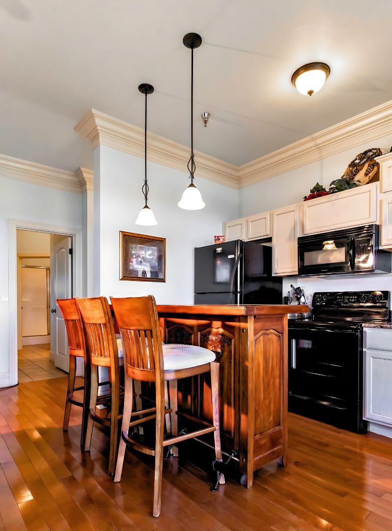 A kitchen with a wooden island, bar stools, a refrigerator, a stove, and pendant lighting.