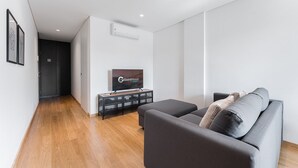 Un salon moderne avec un canapé gris, un téléviseur à écran plat et un meuble de rangement noir pour les appareils multimédias.
