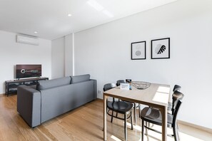Ett modernt vardagsrum med en grå soffa, ett matbord i trä med fyra stolar och en platt-TV placerad på ett TV-bord.