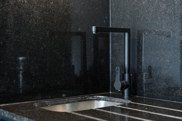 A modern kitchen with a black countertop and a stainless steel sink. - GuestReady - Poet's Modern Retreat (Porto)