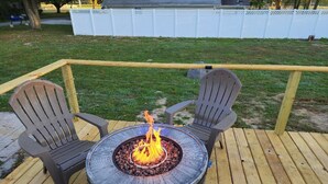 A round fire pit table with two Adirondack chairs on a wooden deck. - Harmony House (Kokomo)