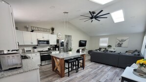 A modern kitchen with white cabinets, a central island, and a dining area with a table and chairs. - Harmony House (Kokomo)