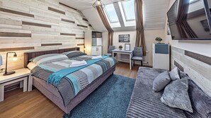 A modern bedroom with a sloped ceiling, a large bed, a desk, a chair, and a television mounted on the wall. - Nestled in the Quiet Hills of Prague, Attic Suite 2 (Hlavní mesto Praha)