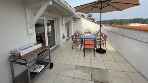 A patio with a table and chairs, a large umbrella, and a cart with items on it. - New appartment near the center for 6 people with car park (LACANAU OCEAN)
