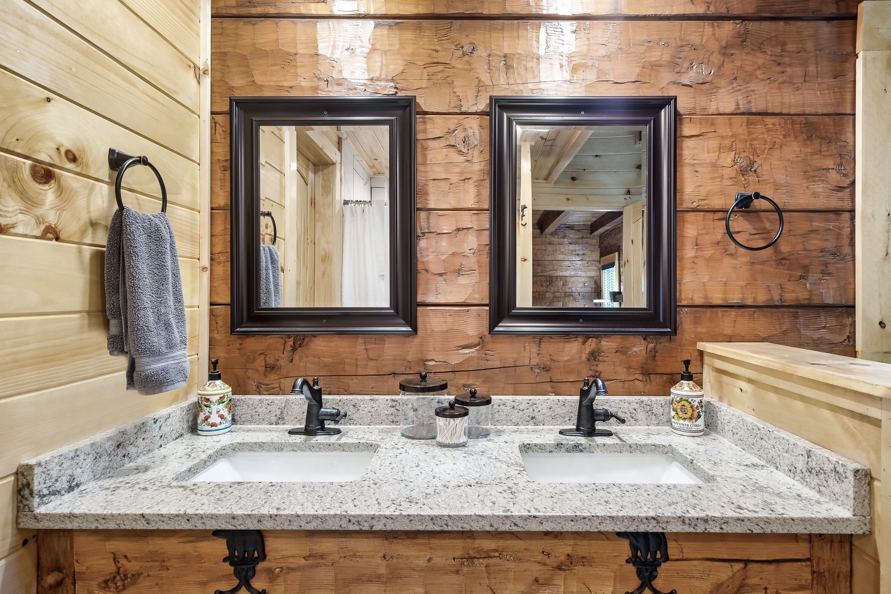A bathroom with wooden walls, two mirrors, a granite countertop, and a sink.