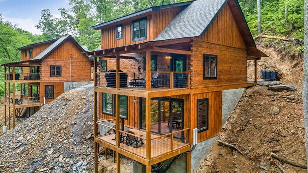 A two-story log cabin with a balcony and a covered deck, surrounded by a forested hillside. - Rustic 2BR Log Cabin w/ Private Indoor Pool & Hot Tub — Near Pigeon Forge (Sevierville)