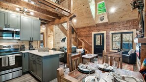 A spacious kitchen with modern appliances, a dining area with a wooden table set for four, and a cozy living room with a fireplace. - Rustic 2BR Log Cabin w/ Private Indoor Pool & Hot Tub — Near Pigeon Forge (Sevierville)