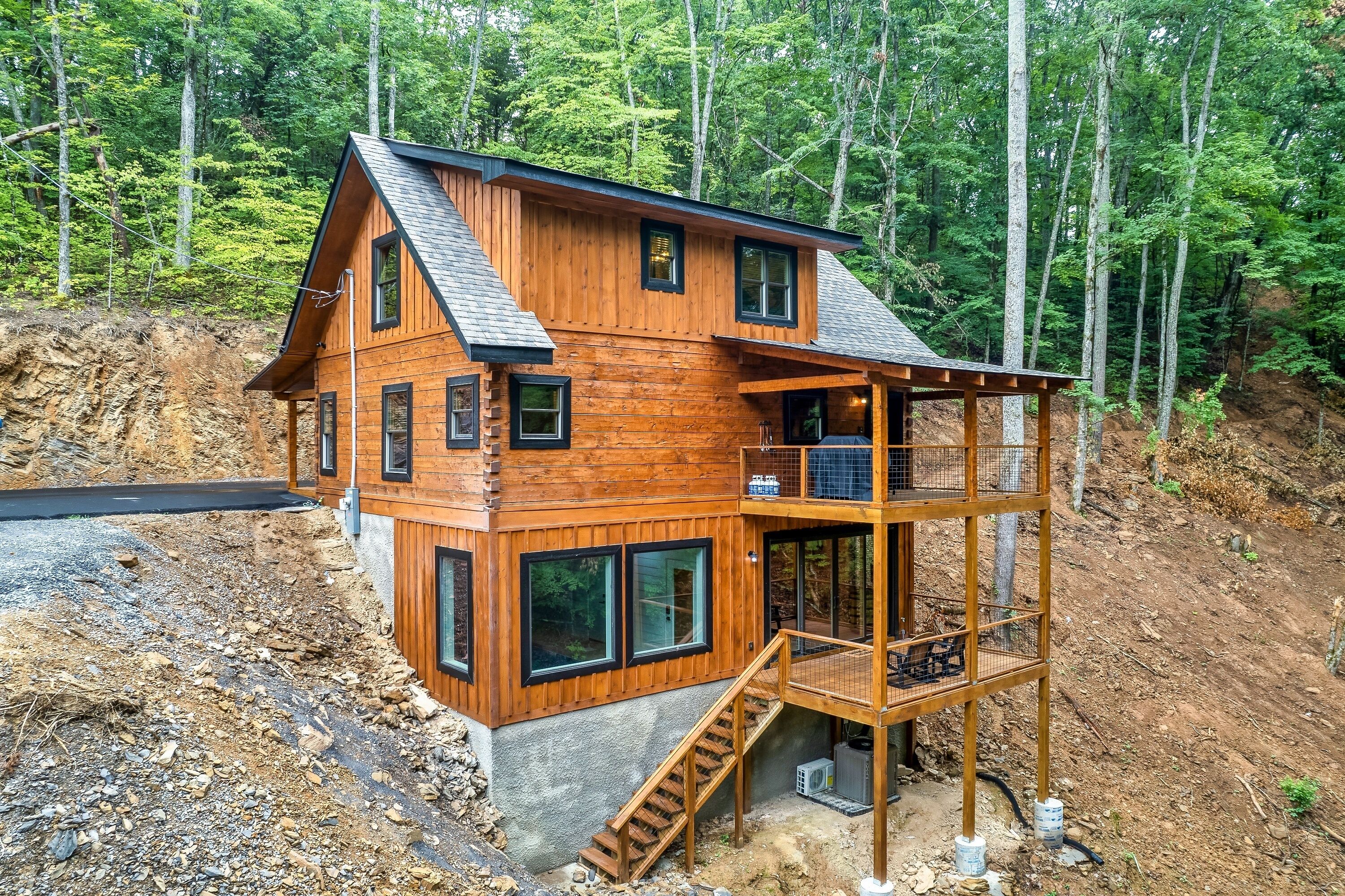 Een houten vakantiehuis met meerdere verdiepingen en een balkon, omgeven door bos.