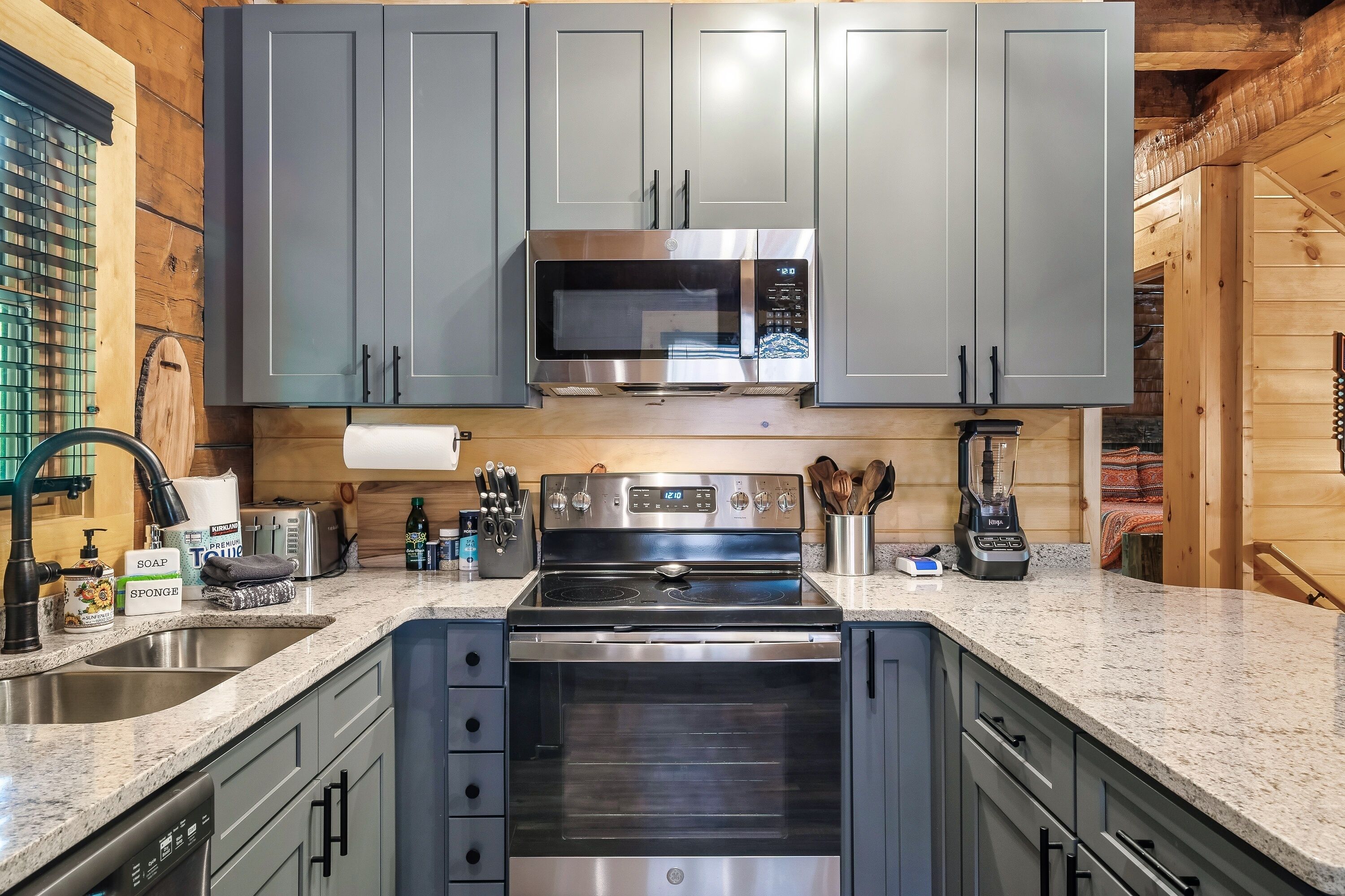 A modern kitchen with grey cabinets, stainless steel appliances, and a granite countertop.