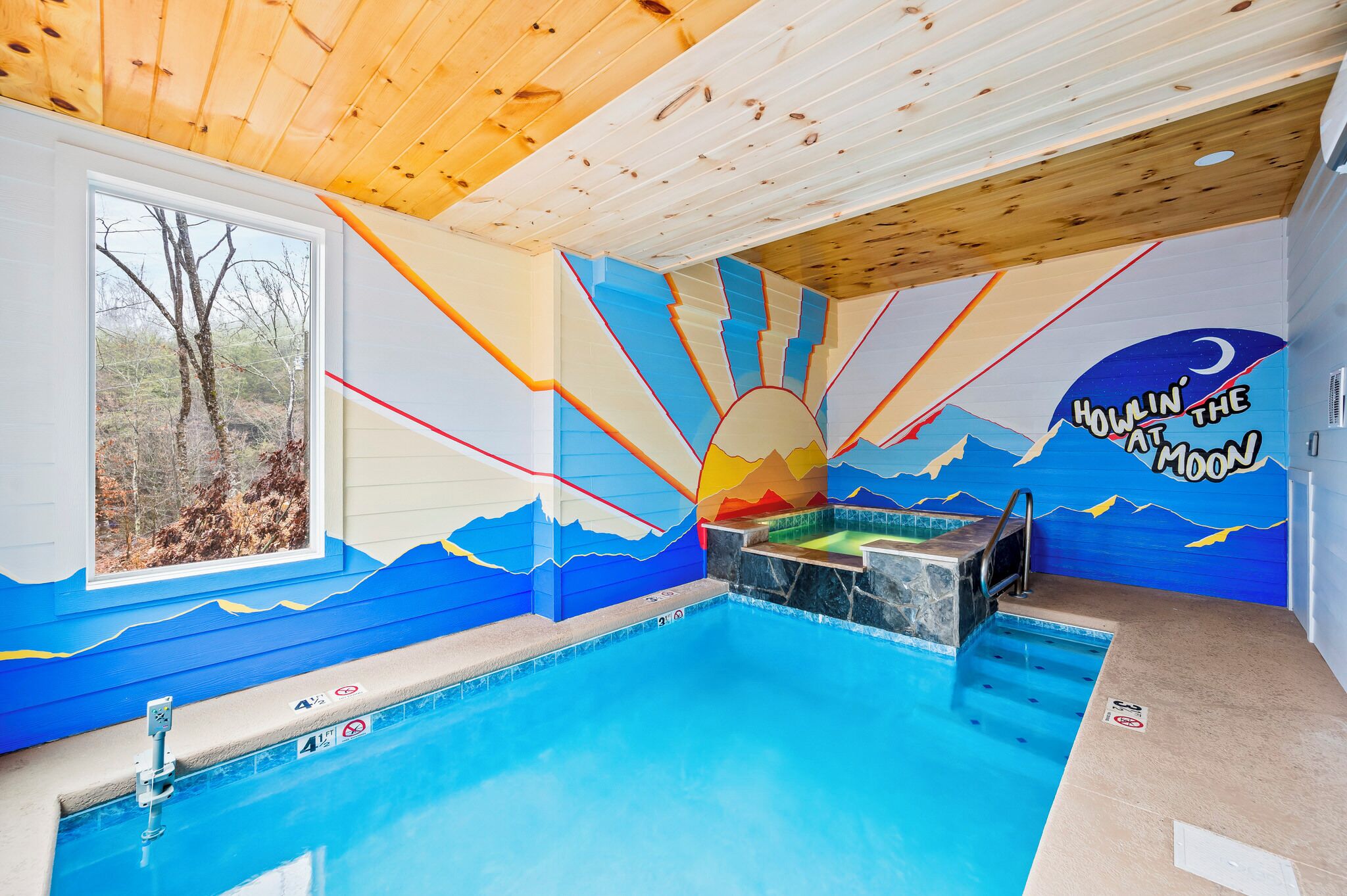 Une piscine ornée d’une fresque représentant un soleil et des montagnes, avec un plafond en bois et une fenêtre donnant sur la forêt.