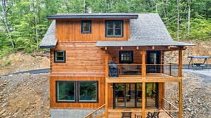 Eine zweistöckige Holzhütte mit Balkon und Terrasse, umgeben von Wald.
