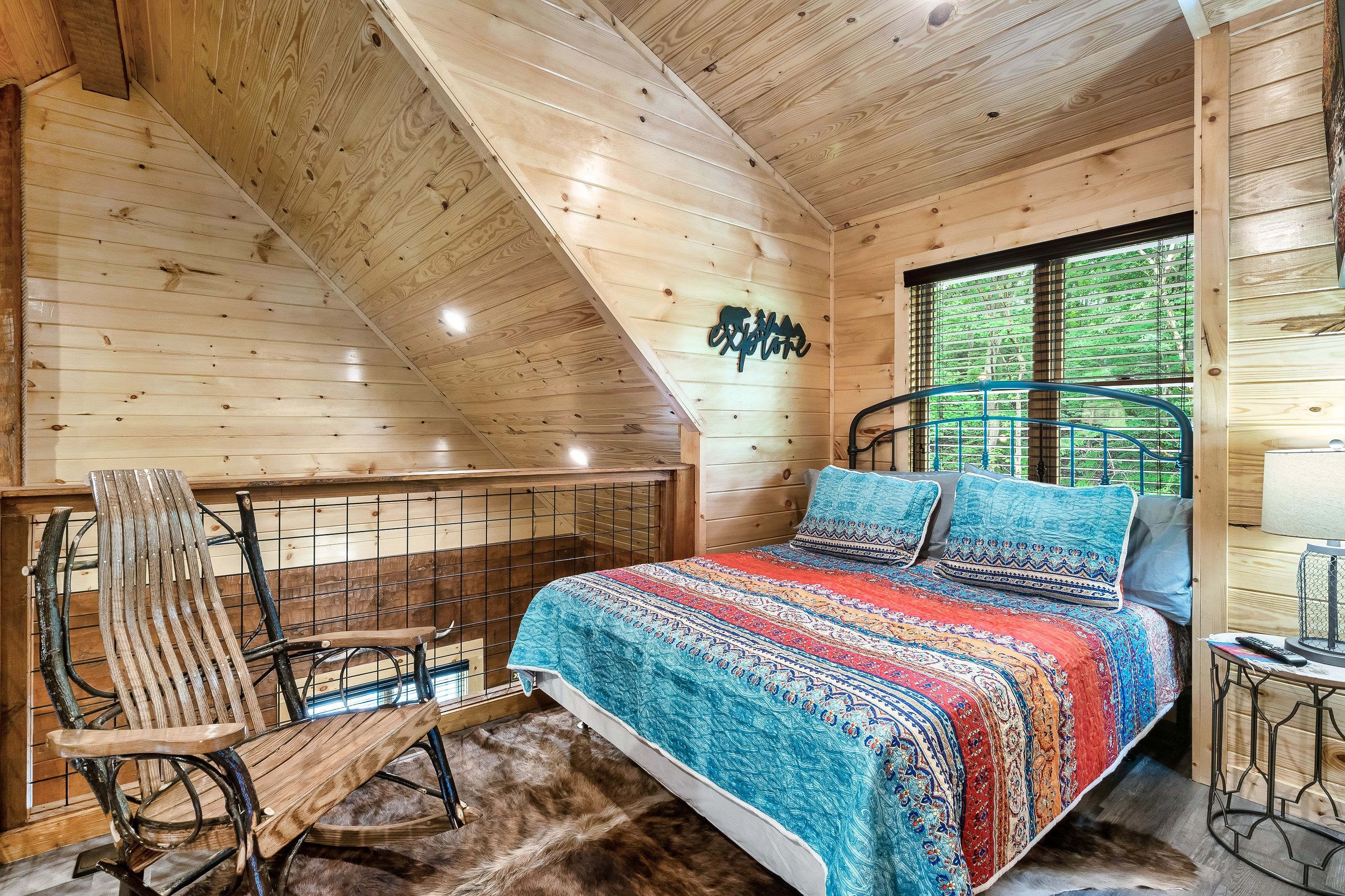 A wooden cabin bedroom with a bed, a chair, a small table, and a window with blinds.