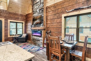 Un intérieur rustique en bois, avec une cheminée, un téléviseur, une table à manger dressée pour quatre personnes et un coin salon confortable.