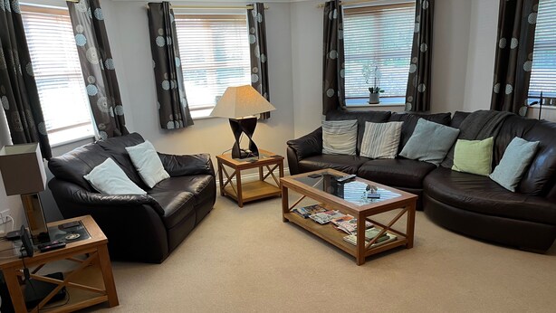 A living room with two leather sofas, a wooden coffee table, a lamp, and a TV stand. - Captivating Apartment Near Gatwick (Crawley)
