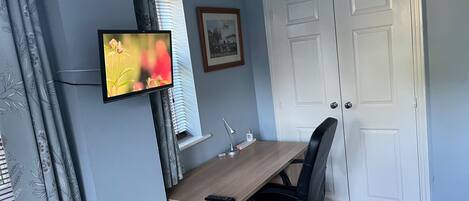 A room with a desk, a chair, a television, a door, and a window with curtains.