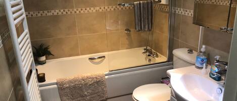 Un baño con bañera, inodoro y lavamanos, equipado con dispensador de gel antibacterial y un perchero para toallas.