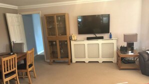 A living room with a television, a cabinet, a desk, and a chair. - Captivating Apartment Near Gatwick (Crawley)