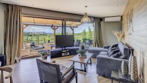 A spacious living area with a large flat-screen TV, comfortable seating, and a view of a lush landscape. - 2-bed Pool Villa in Panormo (Mylopotamos)