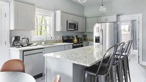 Una cocina moderna con armarios blancos, encimera de granito, electrodomésticos de acero inoxidable y una zona de bar con taburetes.