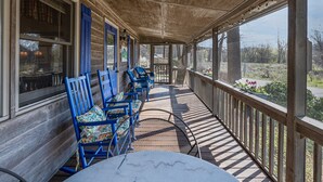 A covered porch with blue chairs and a table, overlooking a garden with flowers and trees. - Still Standing! Cozy Cottage, Incredible Location! (Lake Lure)