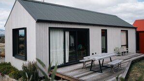 Una casa moderna con terraza de madera, grandes puertas correderas de vidrio y techo de metal.