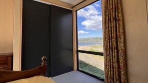 Un dormitorio con cama, ventana con cortinas y vista a un paisaje.