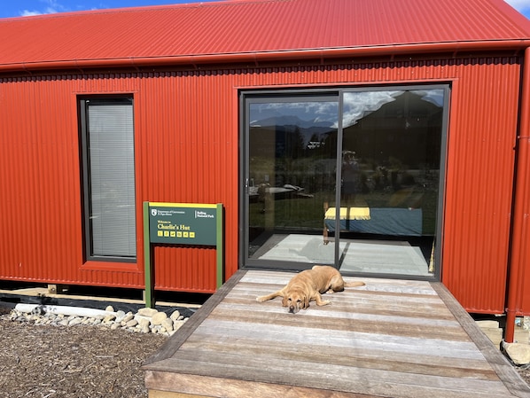 Een rood gebouw met een grote glazen deur en een houten hellingbaan die ernaar leidt. Een bord ervoor zegt: "Welkom bij Charlie's Hut".
