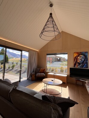 Een moderne woonkamer met een groot raam, een bank, een bijzettafeltje en een schilderij aan de muur.