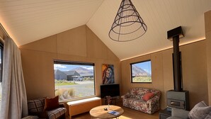 Un salón acogedor con techo de madera, un ventanal con vistas a montañas, un sofá, una mesa de centro y una chimenea.