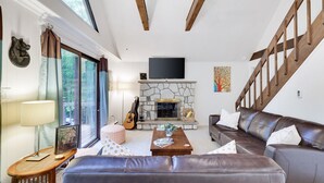 Una sala de estar con chimenea de piedra, un televisor montado encima y un sofá de cuero marrón, además de una mesa de centro de madera.