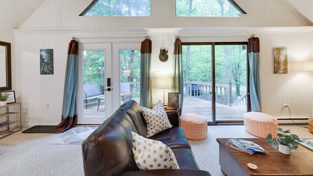 Amplia sala de estar con sofá de cuero, una mesa de centro y una estantería. Cuenta con ventanas grandes con cortinas, chimenea y vistas a una terraza.