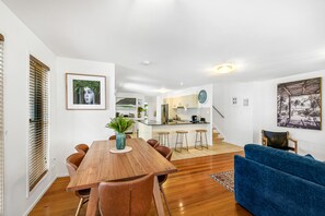 A modern kitchen with a central island, a dining area with a wooden table and chairs, a blue sofa, and a staircase leading to an upper level. - Little Fern House a Tropical Beach Hideaway Mudjimba,  Sunshine Coast 🛫 5 mins (Mudjimba)