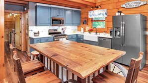 A rustic kitchen with a wooden table and chairs, blue cabinets, a stainless steel refrigerator, and a 'Welcome to the Farm' sign. - Gorgeous custom log cabin on 185 acres (Dellrose)