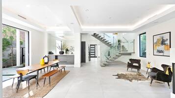 A spacious, modern living area with a large dining table, comfortable seating, a staircase, and a view of the outdoors.