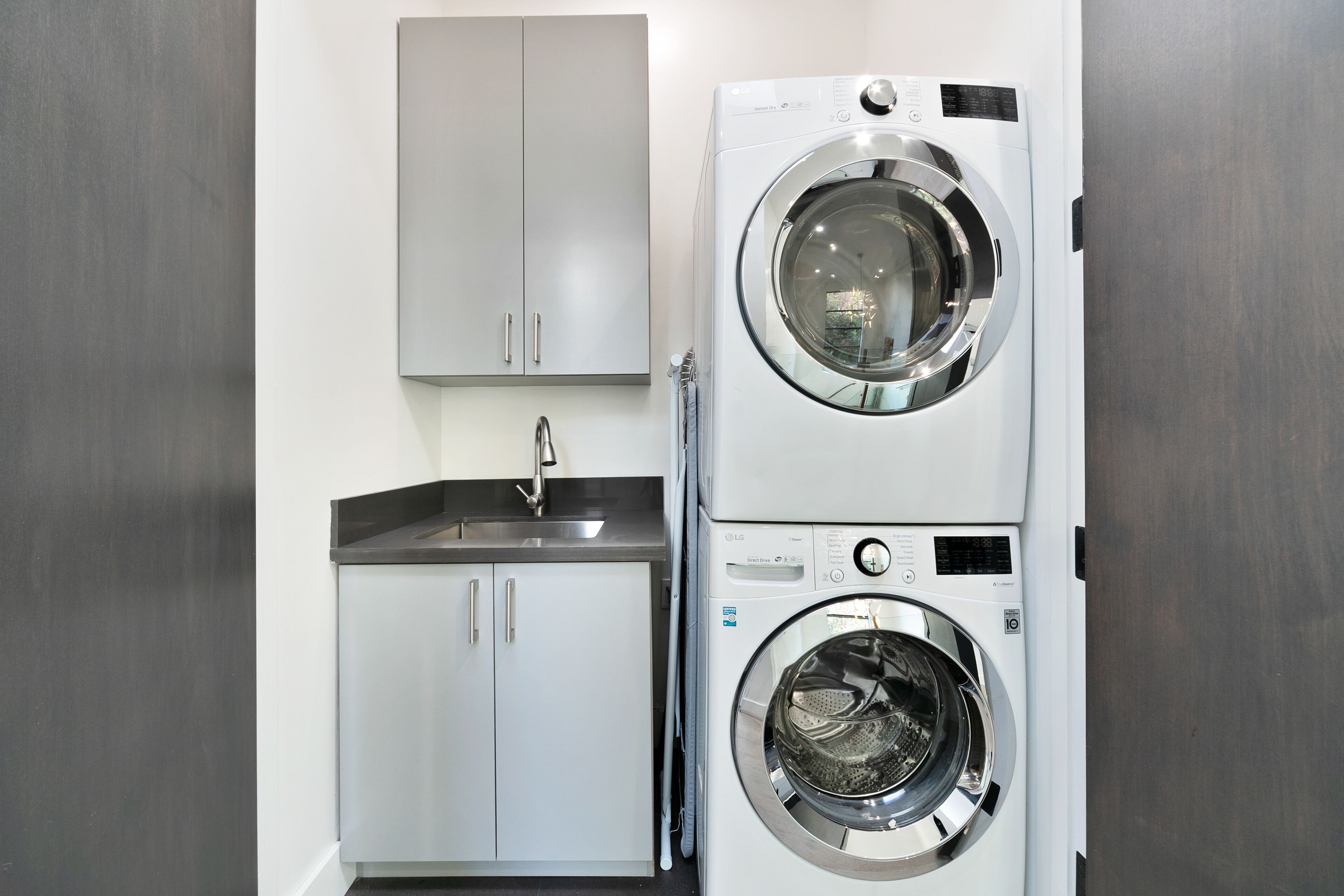A compact laundry area with a double-door washer and dryer, a stainless steel sink, and a white cabinet.