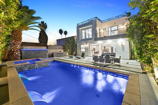 Une maison moderne à deux étages dotée d’une piscine, d’un espace salon extérieur et d’un balcon.