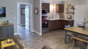 A modern kitchen with wooden cabinets, a stainless steel oven, and a dining area with a wooden table and bench. - Restored Building in Downtown Lincoln- Your Gateway to the Lake! (Lincoln)