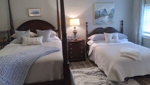 A bedroom with two single beds, a nightstand with a lamp, a painting on the wall, and a window with curtains. - Restored Building in Downtown Lincoln- Your Gateway to the Lake! (Lincoln)