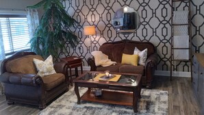 A living room with a brown leather sofa, a glass coffee table, and a large potted plant. - Restored Building in Downtown Lincoln- Your Gateway to the Lake! (Lincoln)