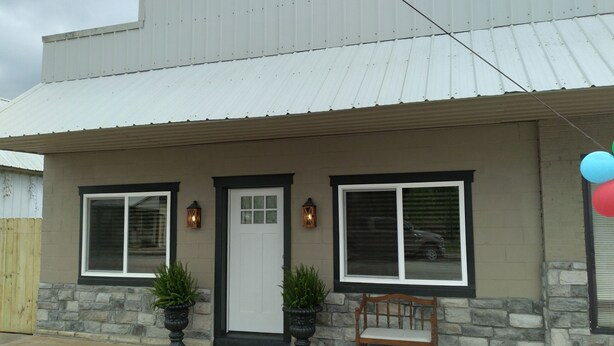 A two-story building with a metal roof, a front door, two windows, and a bench outside. - Restored Building in Downtown Lincoln- Your Gateway to the Lake! (Lincoln)