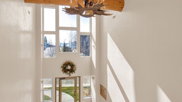 Eine Holztreppe mit Holzwertung, eine Holzbalkendecke mit Leuchte und Blick ins Freie durch große Fenster.