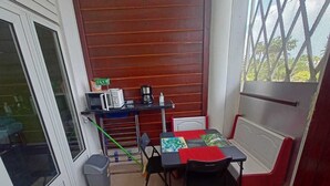 A small, enclosed balcony with a table and chairs, a coffee maker, and a trash bin. - 1 Bedroom Apartment in Le Moule (Le Moule)