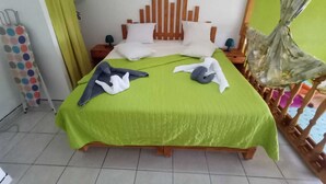 A bed with a green bedspread, wooden headboard, and white pillows. There are two bedside tables with lamps. - 1 Bedroom Apartment in Le Moule (Le Moule)