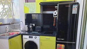 A compact kitchen with a washing machine, a coffee maker, and a refrigerator. - 1 Bedroom Apartment in Le Moule (Le Moule)