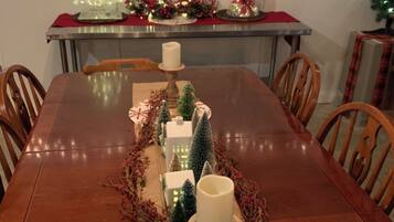 A dining table with a centerpiece featuring candles, miniature Christmas trees, and a garland.